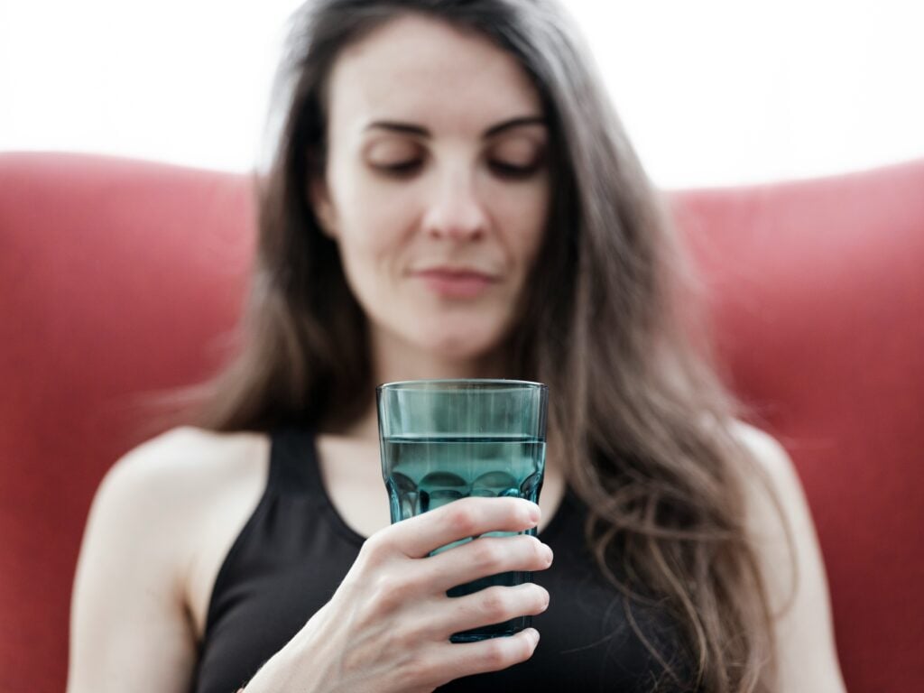 woman looking at a glass of drinking water wondering what is in it and if it is safe to drink